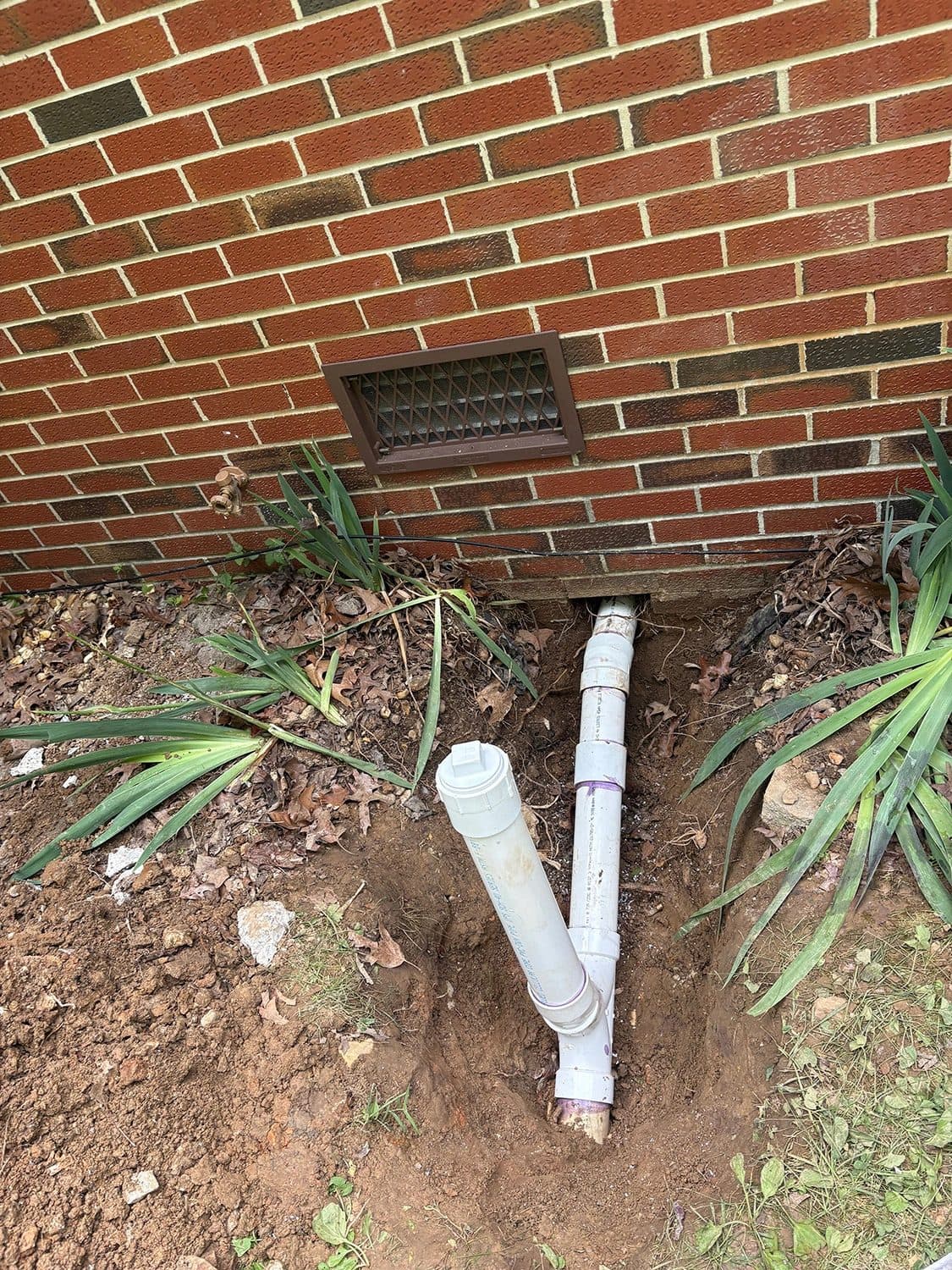Sewer cleanout pipe installed in freshly dug soil beside a brick home